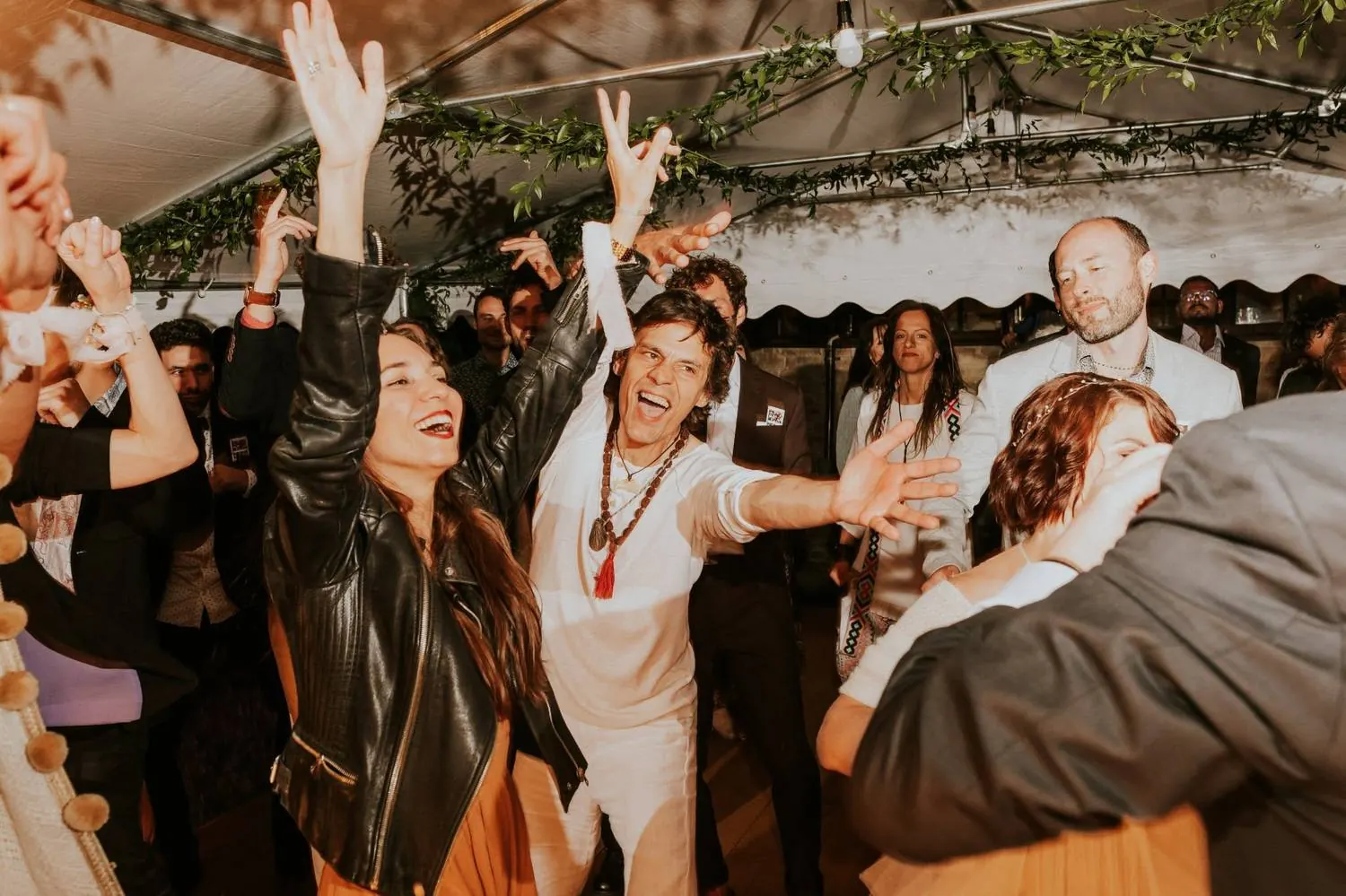 Guests dancing with raised arms under a marquee